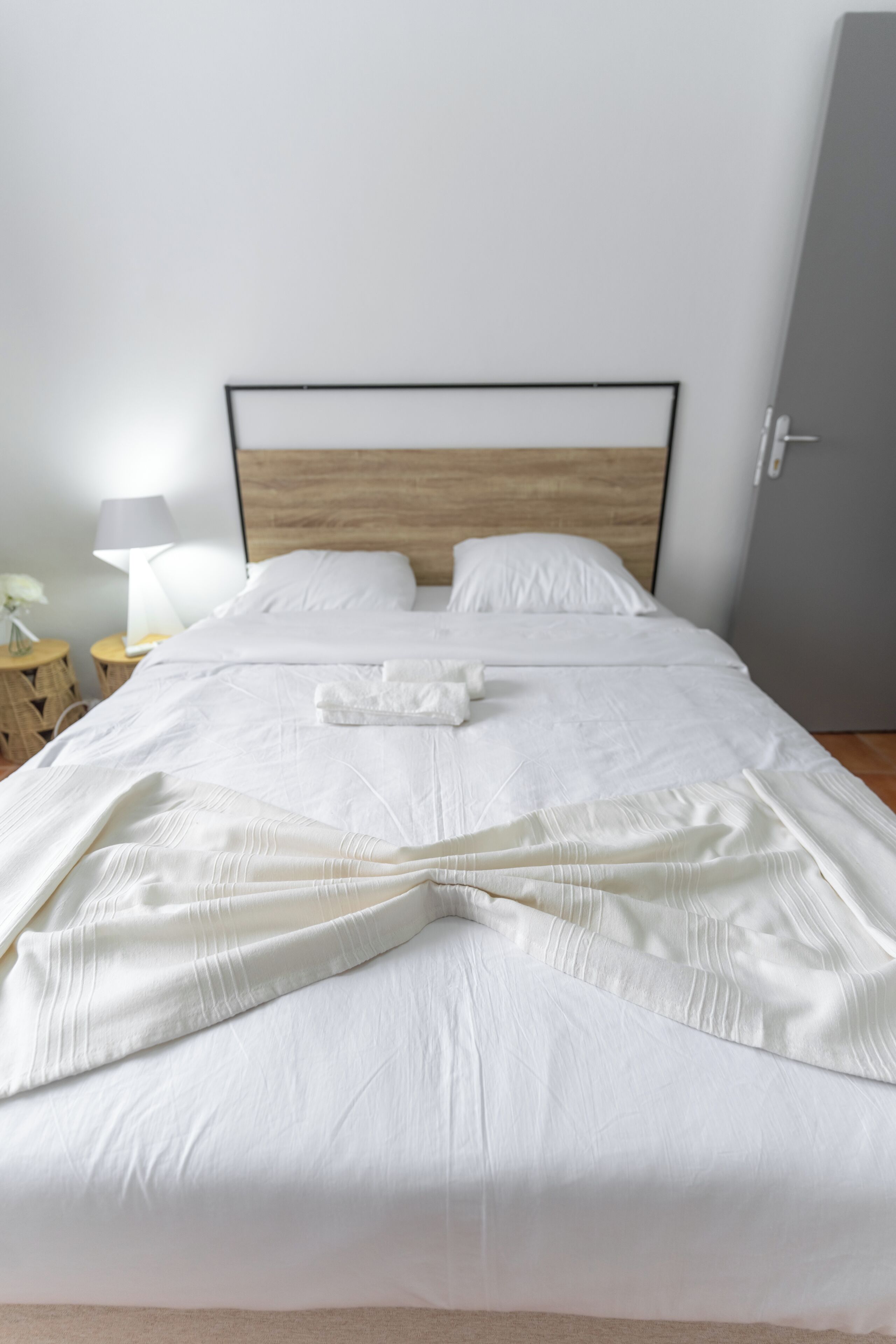 A neatly made bed with white linens, a wooden headboard, and a bedside table with a lamp.