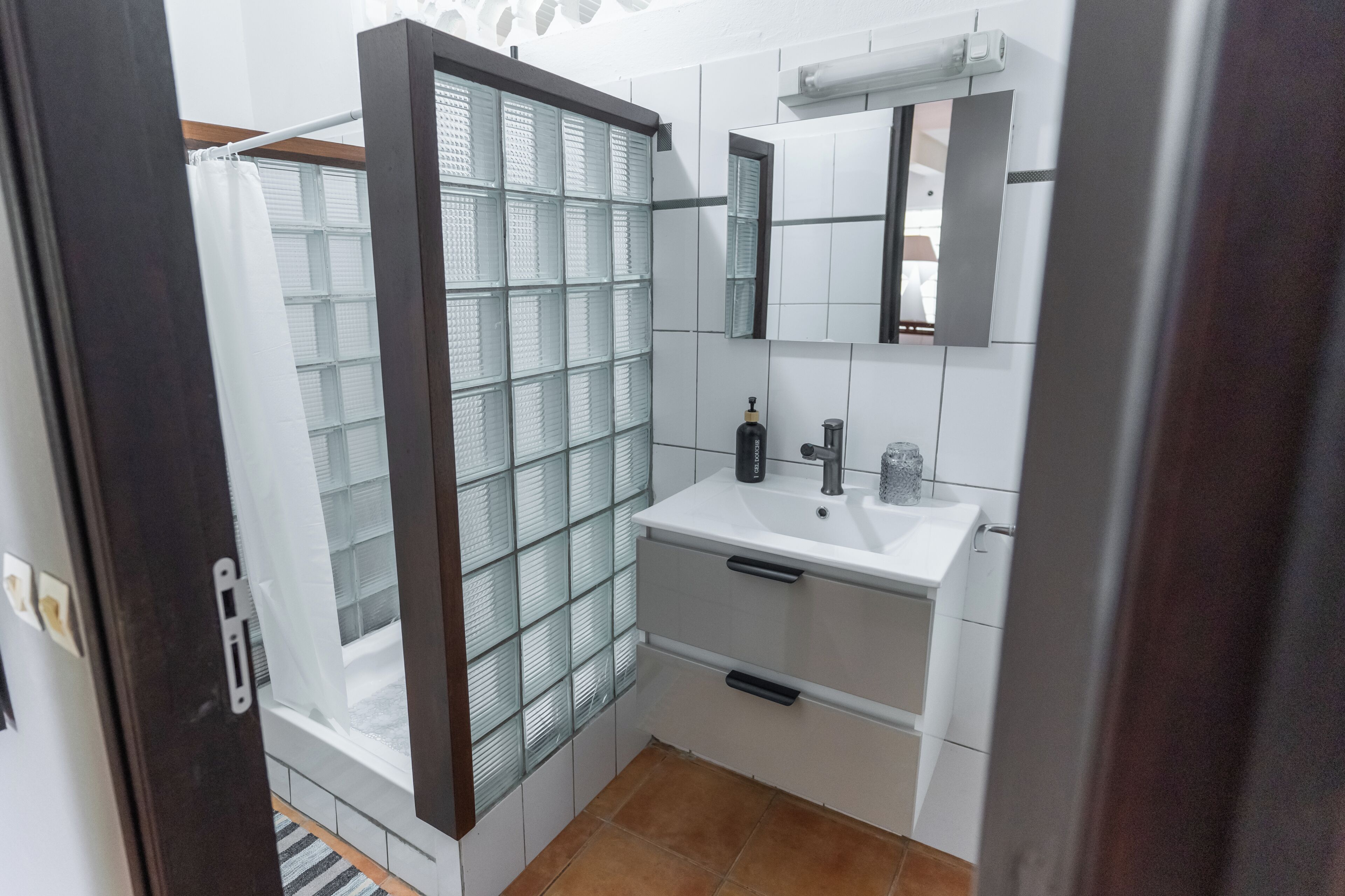 Une salle de bain avec une douche à parois de verre, un lavabo blanc, un miroir et un porte-serviettes.