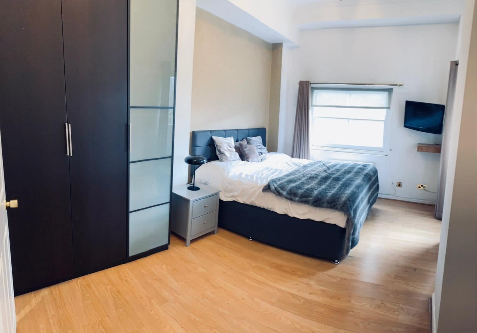 A bedroom with a bed, nightstand, wardrobe, and a TV.