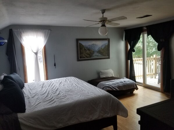 A bedroom with a bed, a bedside table, a ceiling fan, a window with curtains, and a painting on the wall.