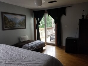 A bedroom with a bed, a painting, a sliding glass door to a balcony, and a desk with a lamp.