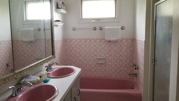 A bathroom with two sinks, a bathtub, a window, and a mirror.