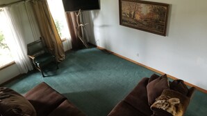 A living room with a large flat-screen TV mounted on the wall, a framed painting, and a brown sofa. - 4BR in Black Creek, near Green Bay Appleton, EAA, hunt, fish, raft, snowmobile (Black Creek)