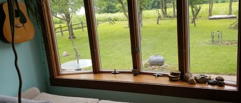 A room with a large window, a guitar, a couch, and a view of a grassy yard.