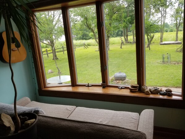 Una habitación con un ventanal grande, una guitarra, un sofá y vistas a un jardín césped.