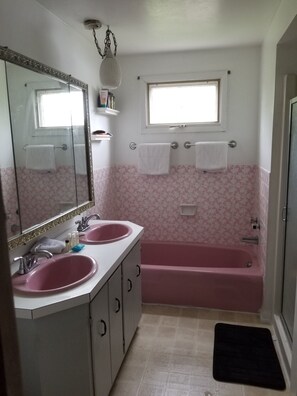 Un bagno con due lavandini, uno specchio grande, una finestra e una vasca da bagno rosa.