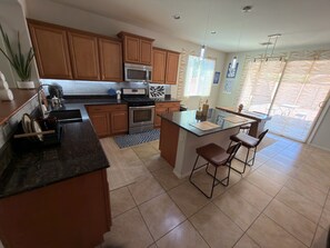 Una cocina con gabinetes de madera, microondas, horno, pileta y una zona de bar con taburetes.