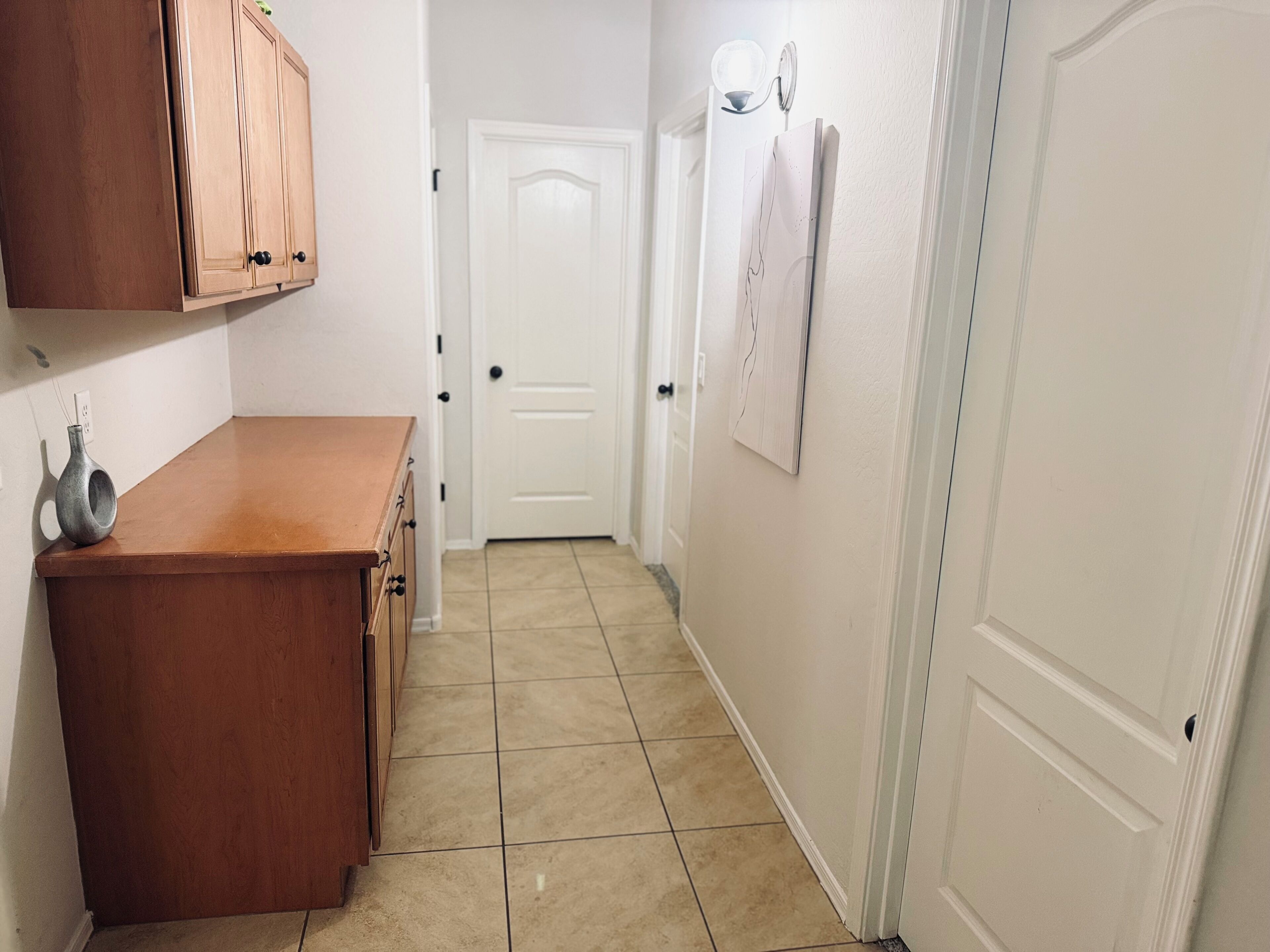 A narrow hallway with a wooden counter, a white door, and a wall-mounted light fixture.