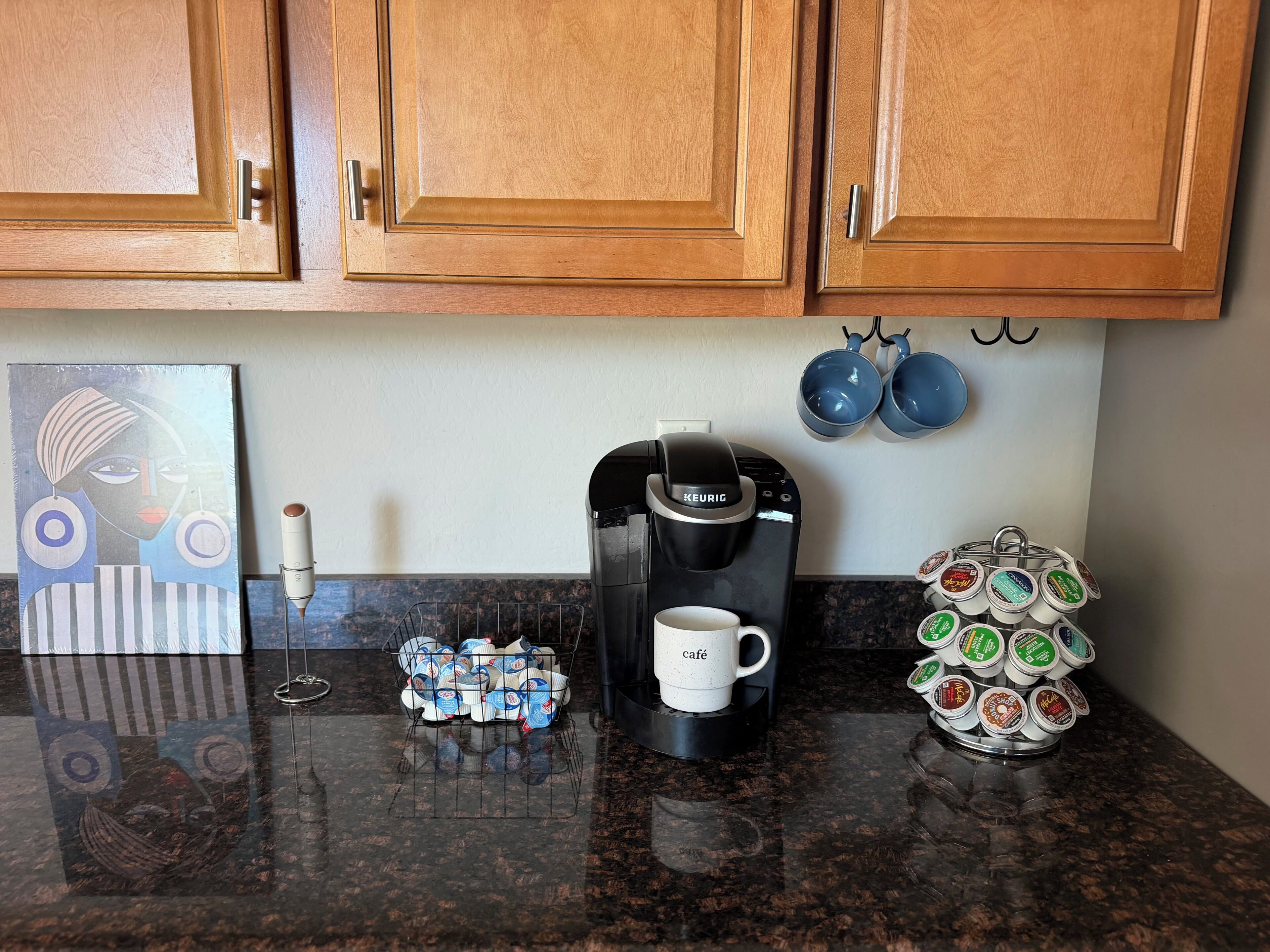Una cocina con armarios de madera, una cafetera, una taza y un portavasos con varias tazas.