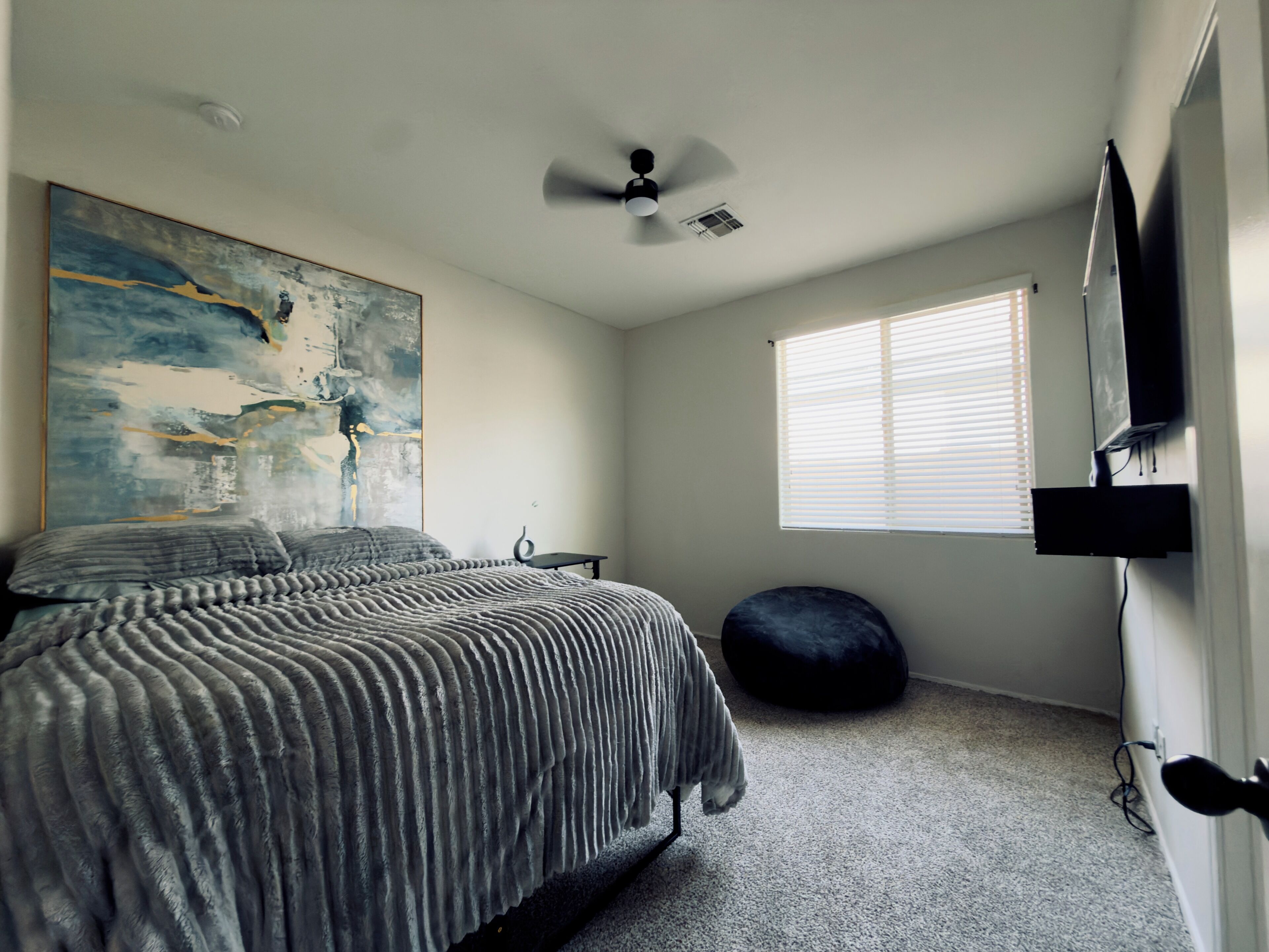 A bedroom with a bed, a ceiling fan, a window with blinds, and a painting on the wall.