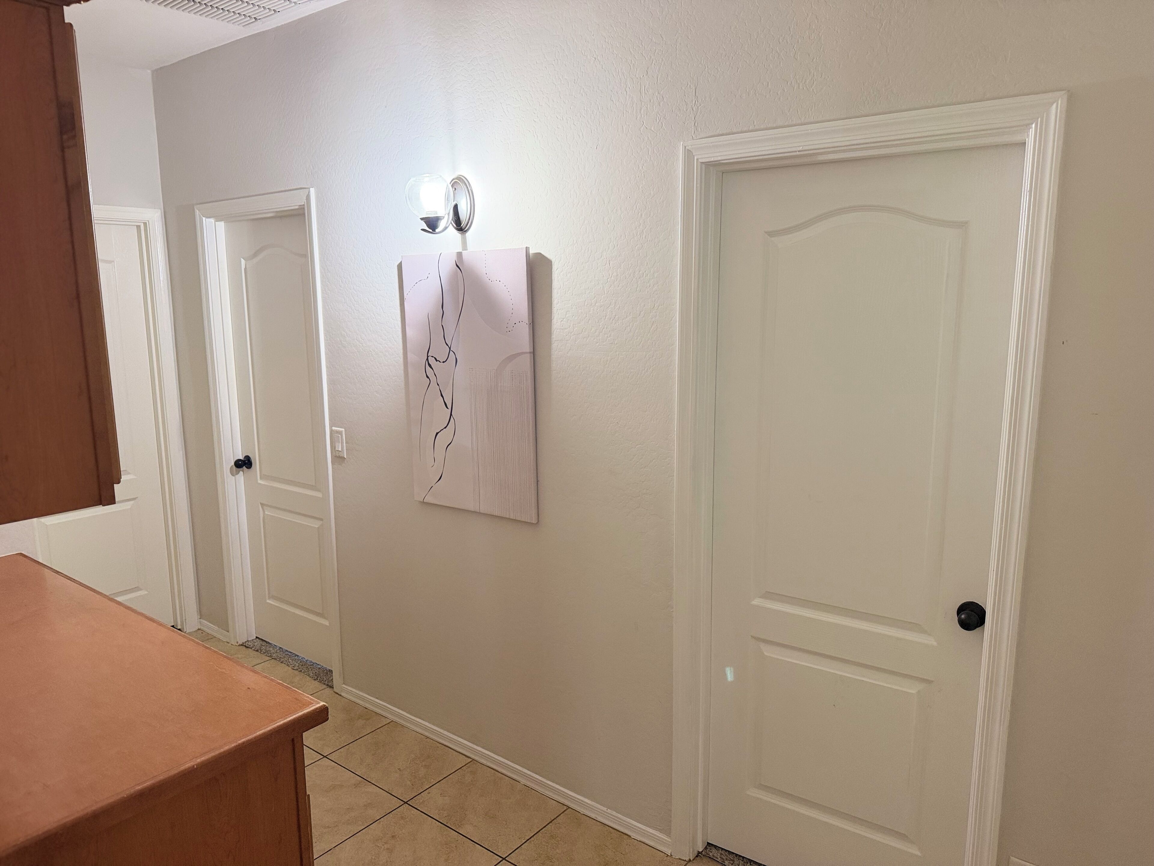 A hallway with three white doors, a wall-mounted light fixture, and a wooden bench.