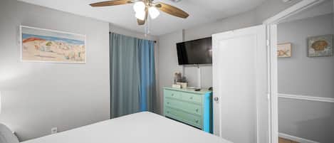 A bedroom with a bed, a ceiling fan, a television, a dresser, and a door.