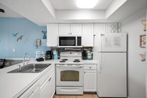 A kitchen with white cabinets, a stove, a microwave, and a refrigerator. - Gulf Front View + Beach Service + Pool + King Bed (Gulf Shores)