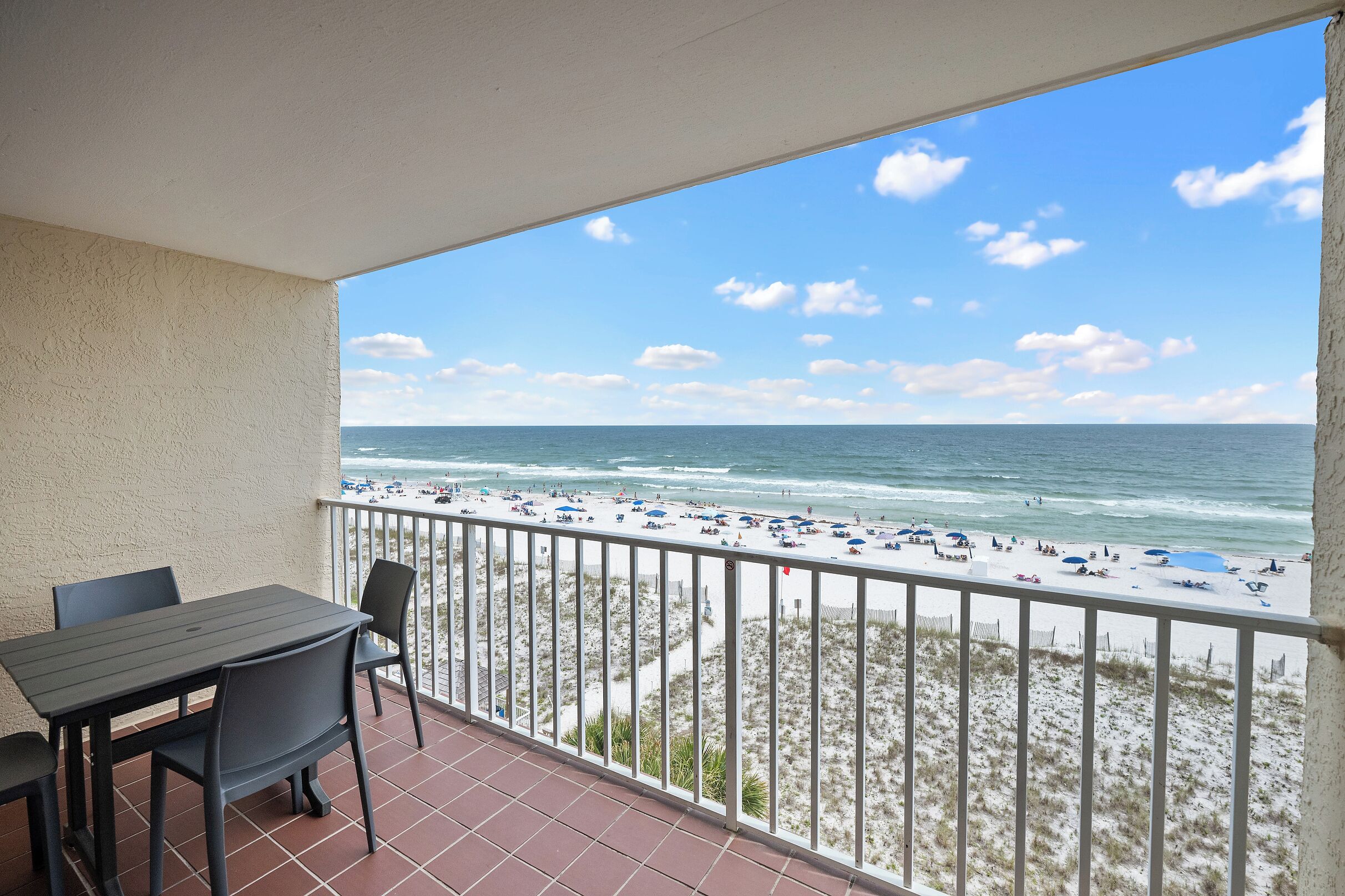 Een balkon met uitzicht op een strand, een tafel en stoelen.