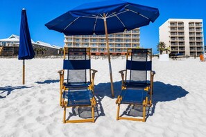 Two beach chairs with a blue canopy and a building in the background. - Gulf Front View + Beach Service + Pool + King Bed (Gulf Shores)