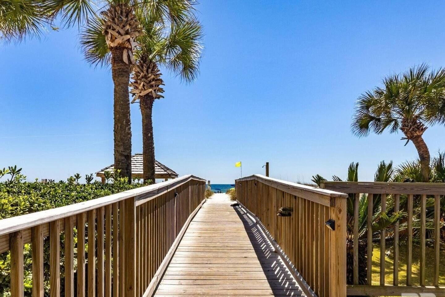 A wooden boardwalk leading to a beach with palm trees on either side.