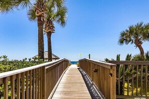 A wooden boardwalk leading to a beach with palm trees on either side. - Gulf Front View + Beach Service + Pool + King Bed (Gulf Shores)