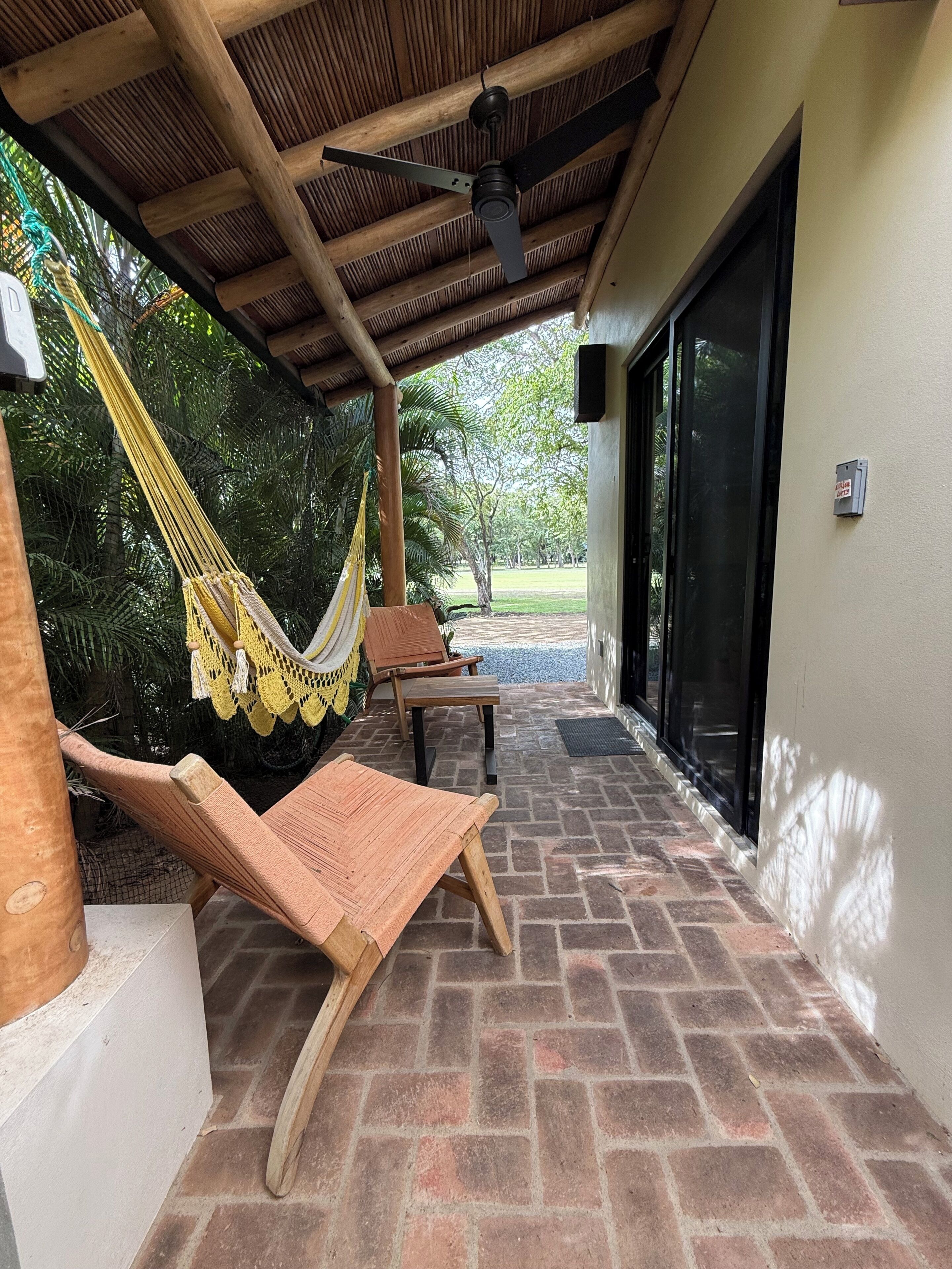 Un espace extérieur abrité, aménagé avec un hamac, des chaises en bois et une table.