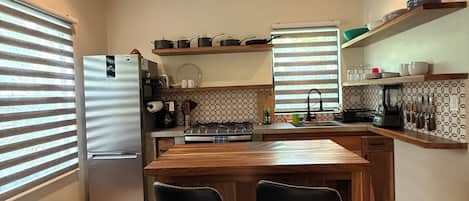 A modern kitchen with a central island, bar stools, a refrigerator, and a ceiling fan.