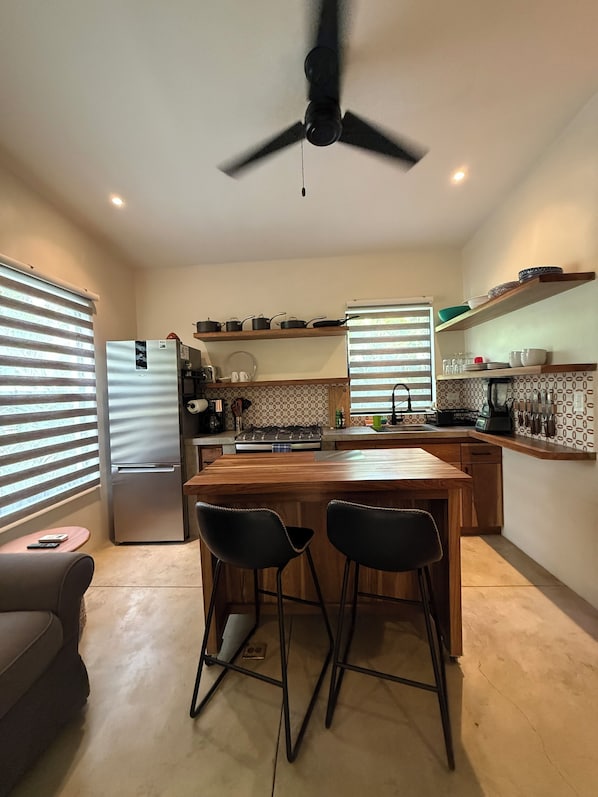 Una cocina moderna con una isla central, taburetes de bar, un refrigerador y un ventilador de techo.