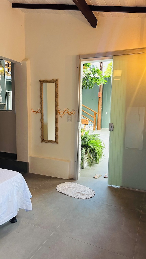 A bedroom with a bed, a mirror, and a door leading to a balcony with plants. - Pousada Refugá (Porto Seguro)