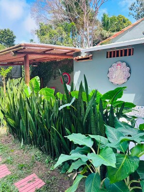A house with a covered porch, a Buddha statue on the wall, and lush green plants. - Pousada Refugá (Porto Seguro)