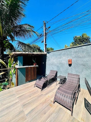 A patio area with two wicker lounge chairs, a small table, and a wooden deck. - Pousada Refugá (Porto Seguro)