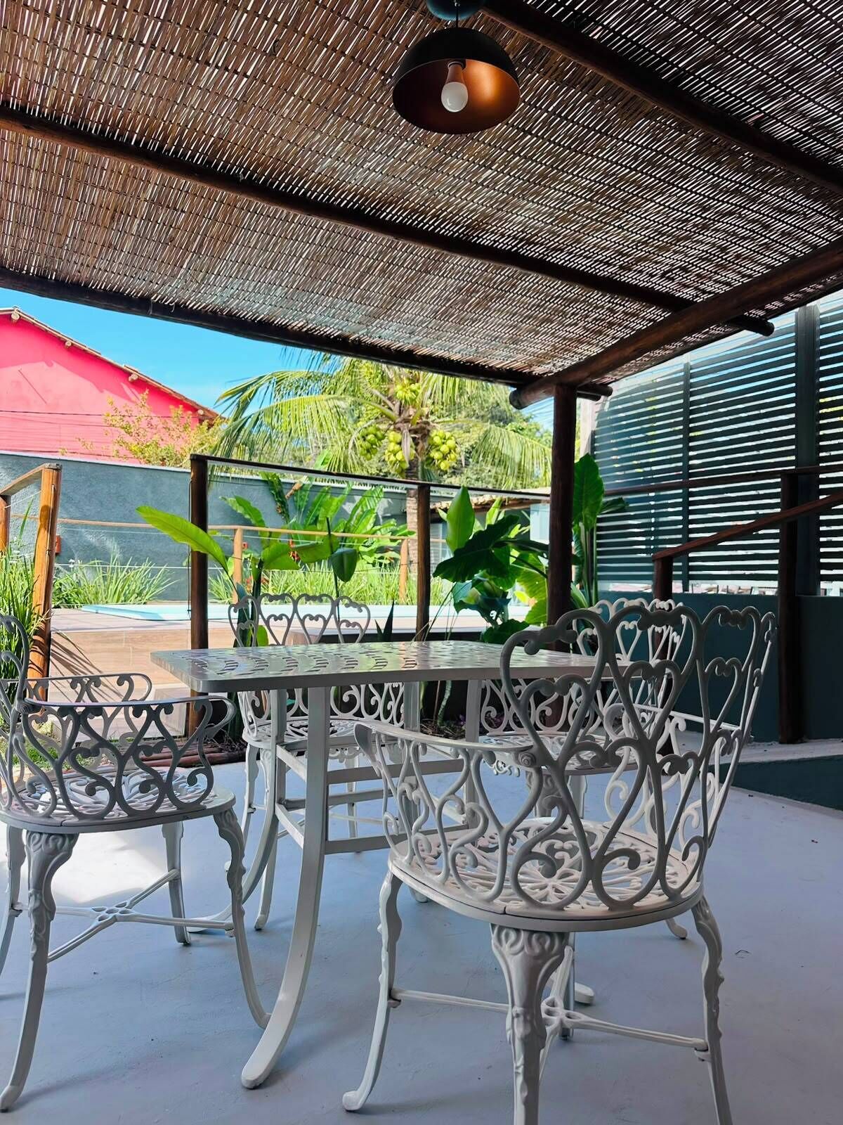 An outdoor patio with a table and chairs, a thatched roof, and tropical plants.