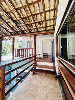A wooden staircase leading to a balcony with a glass railing, a door, and a window with blinds. - Pousada Refugá (Porto Seguro)