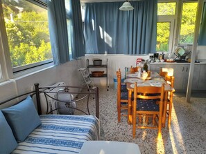 Ein kompakter Raum mit einem Bett, einem Esstisch mit Stühlen, einer kleinen Küchenzeile und Blick ins Grüne.