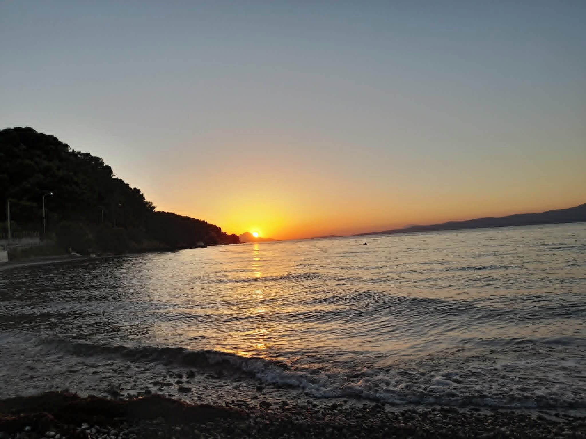 A sunset over a body of water with a rocky shoreline and a hill in the background.
