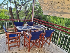 Ein Balkon mit Tisch und Stühlen, umgeben von Grünpflanzen und einem weißen Geländer.