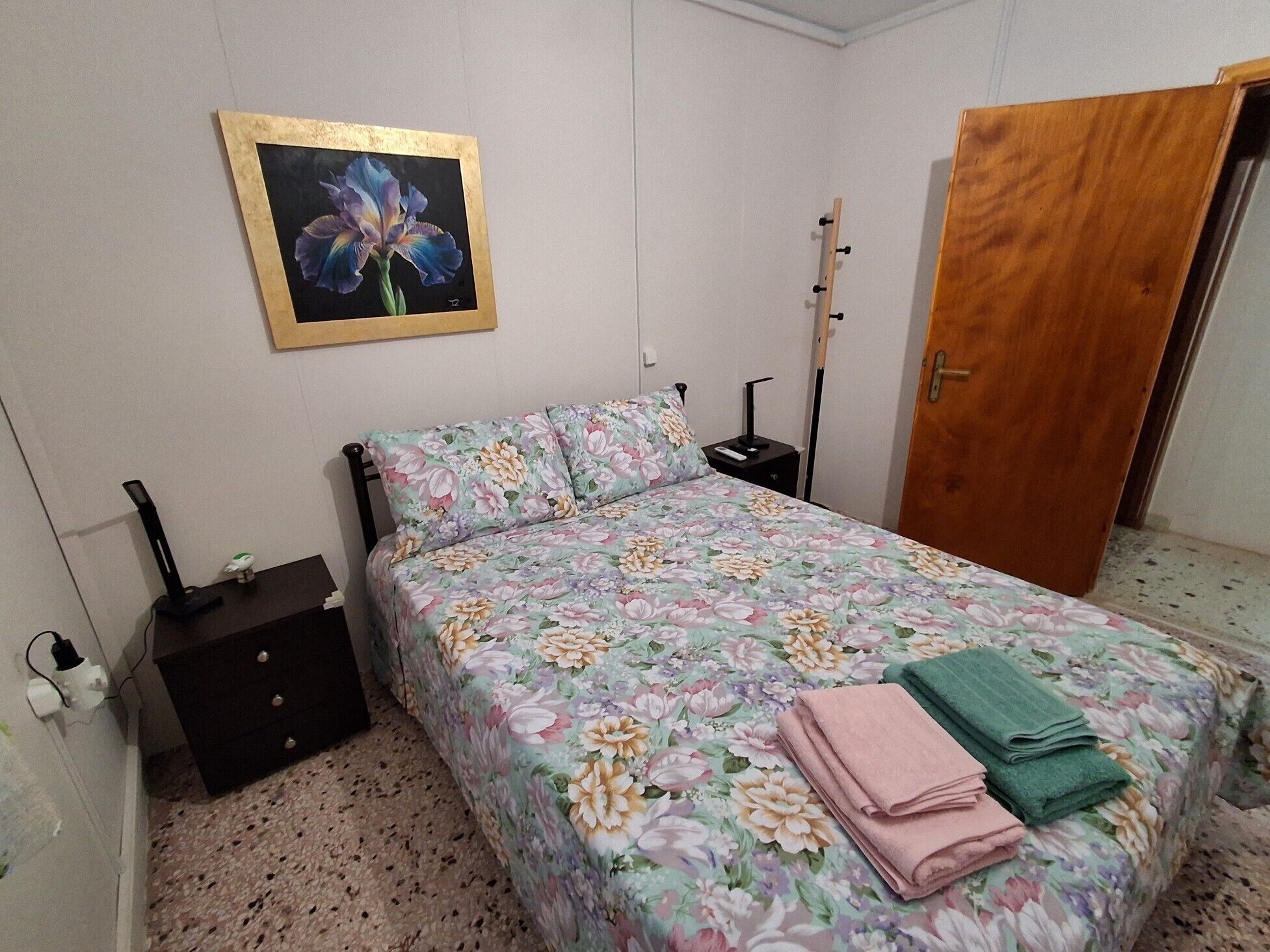 A bedroom with a bed, a nightstand, a dresser, a wooden door, and a framed picture on the wall.