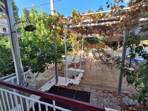 Ein überdachter Außenbereich mit Tischen und Stühlen, umgeben von Bäumen und einer Pergola.