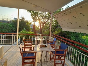 A covered outdoor seating area with tables and chairs, surrounded by a white fence and greenery. - Citrus Garden - Local Culture, Nature, Bikes (Oropos)