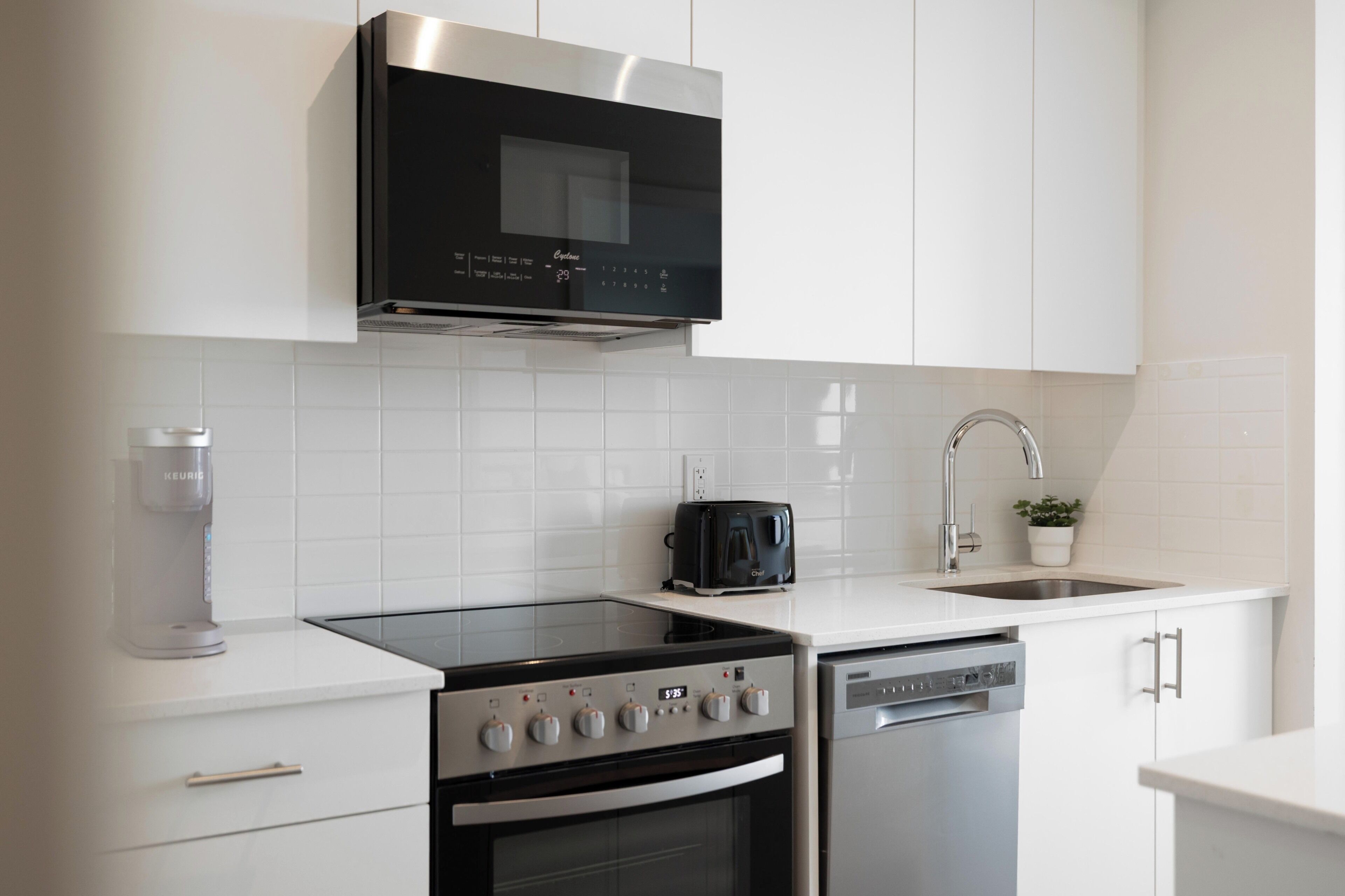 A modern kitchen with white cabinetry, a black range hood, a coffee maker, a toaster, and a dishwasher.
