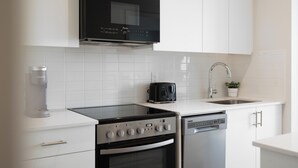 Eine moderne Küche mit weißen Schränken, einer schwarzen Dunstabzugshaube, einer Kaffeemaschine, einem Toaster und einem Geschirrspüler.