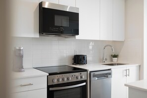 A modern kitchen with white cabinetry, a black range hood, a coffee maker, a toaster, and a dishwasher. - Modern 22nd Floor 1BR | South-Facing City Views | Indoor Parking | North York (Toronto)