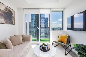Ein modernes Wohnzimmer mit Sofa, Couchtisch und Sessel, mit Blick auf die Stadt durch große Glasfenster.