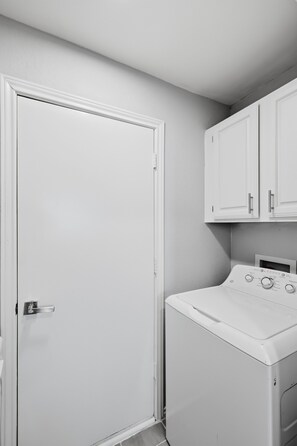 A laundry room with a front-loading washer and dryer, a white door, and a cabinet above the dryer.