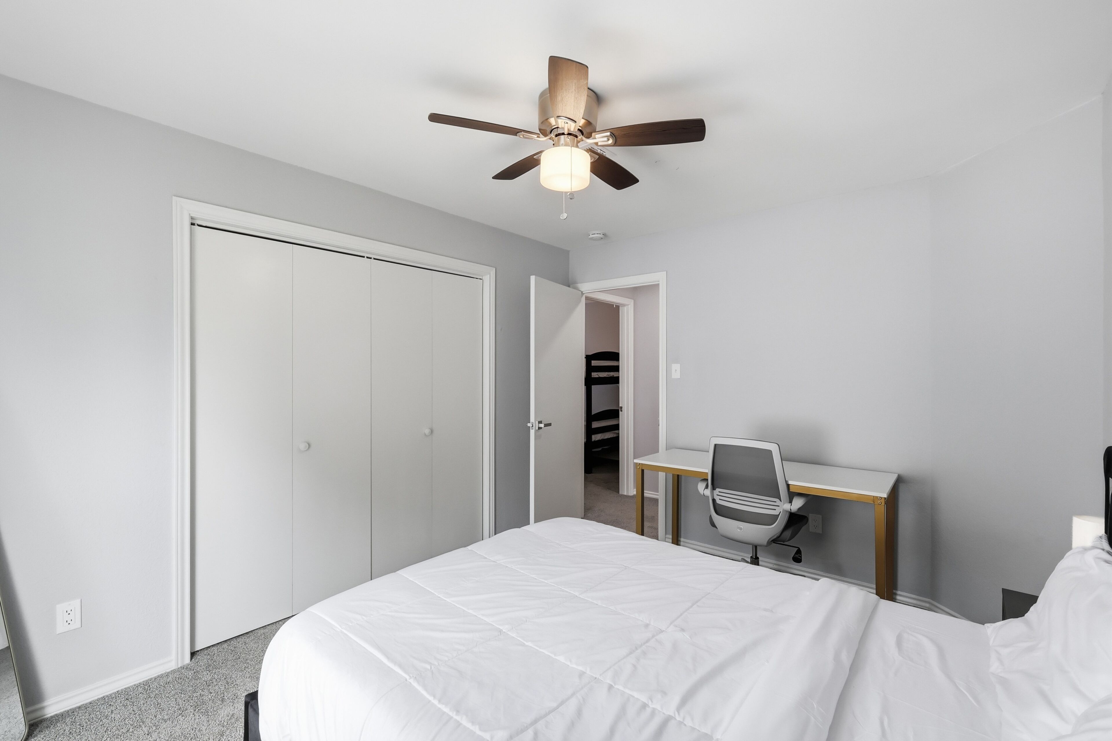 Une chambre à coucher comprenant un lit, un bureau, une chaise, un ventilateur de plafond et un placard.