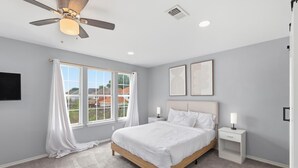 Un dormitorio con cama, ventilador de techo, ventana con cortinas y dos lámparas de noche.