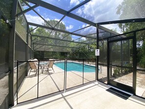 A covered outdoor swimming pool with a glass enclosure, surrounded by chairs and a sign indicating adult supervision is required. - Incredible 5-bedroom POOL Home Next Universal/Parks (Orlando)