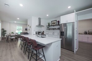 A modern kitchen with a central island, bar stools, a stainless steel refrigerator, and a dining area with a table and chairs.