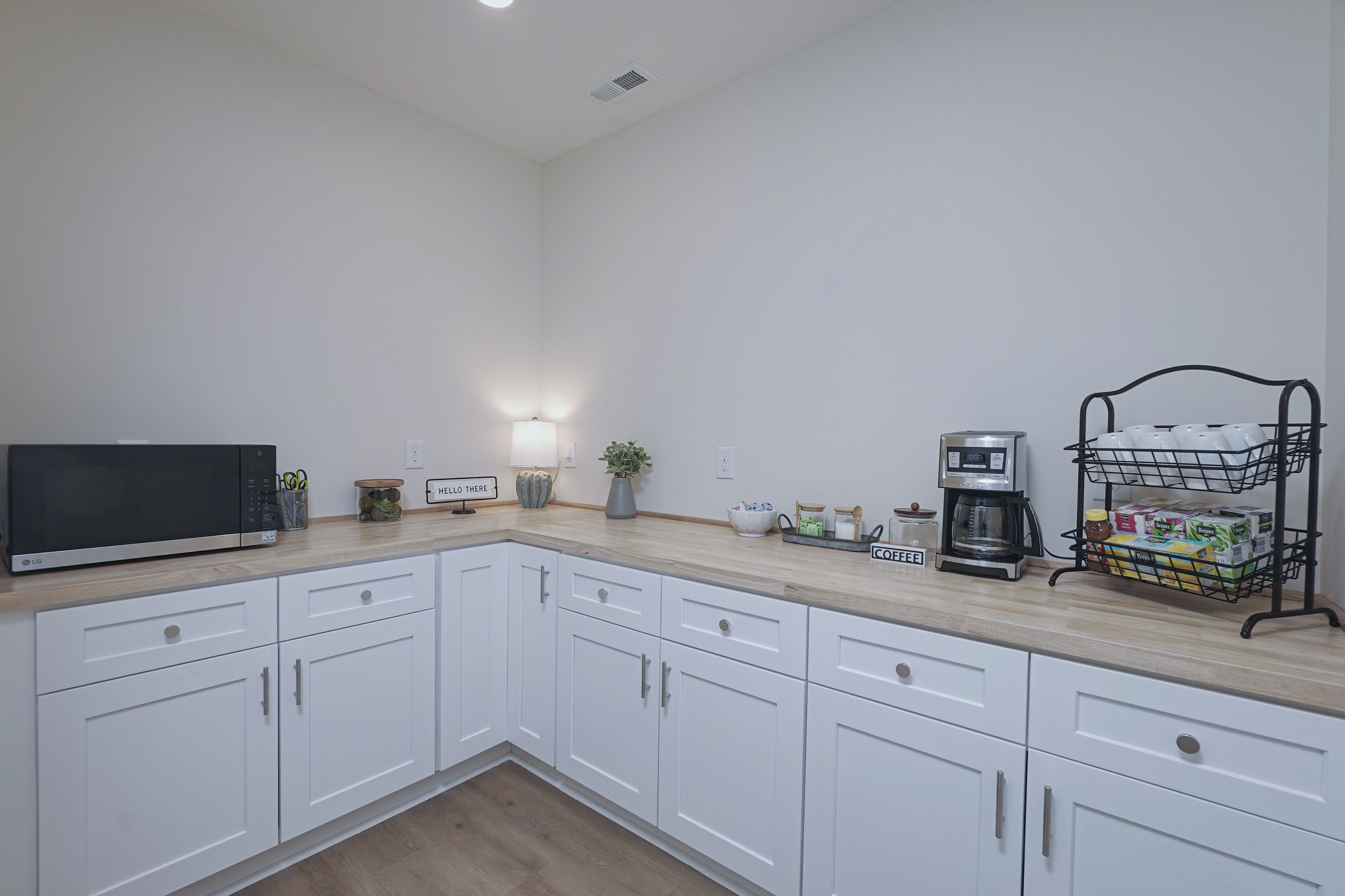A kitchen with white cabinets, a microwave, a coffee maker, and a coffee station.