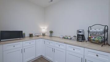 A kitchen with white cabinets, a microwave, a coffee maker, and a coffee station.