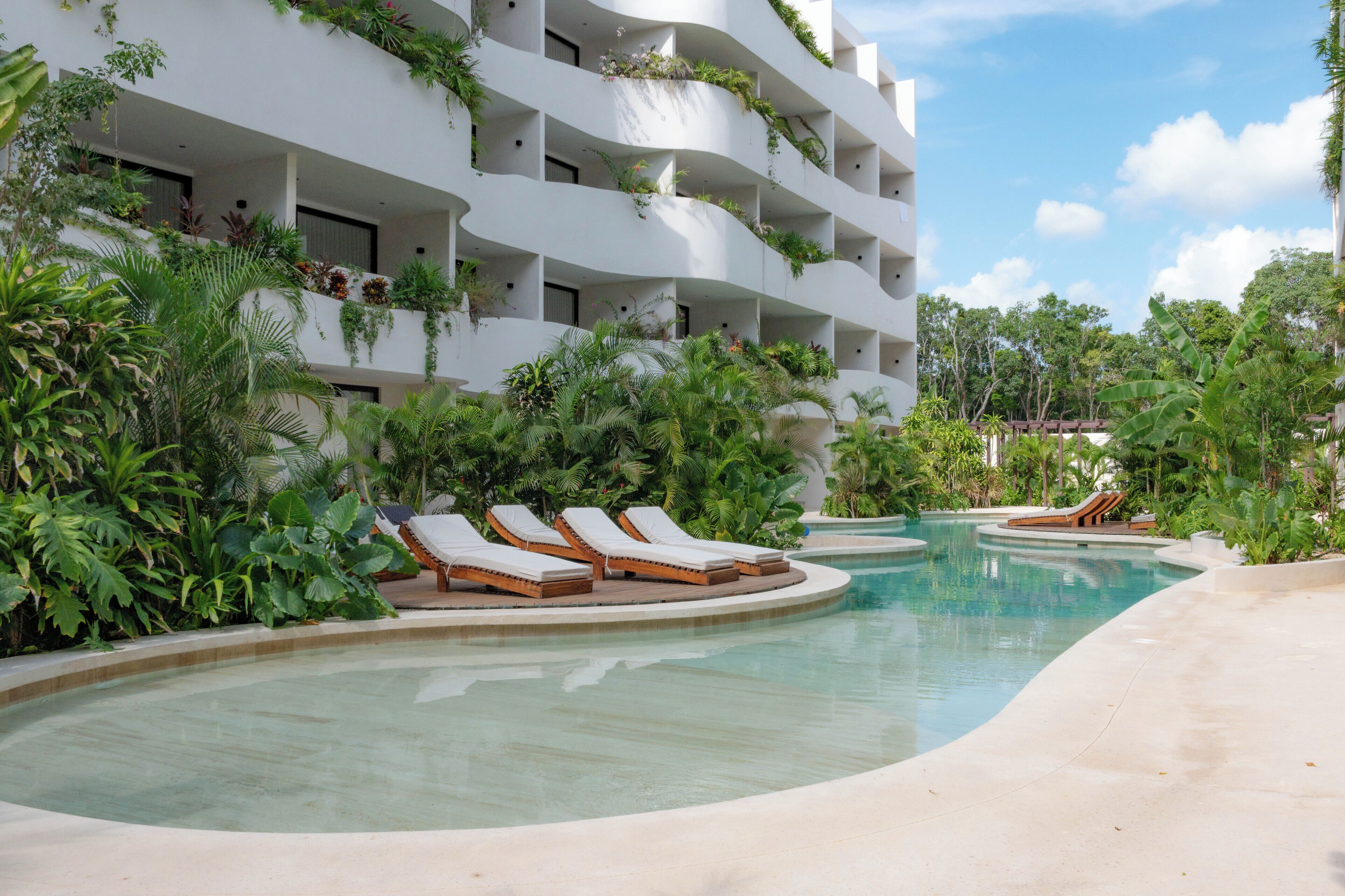 A pool area with lounge chairs and a building with balconies.