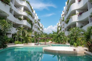 A modern hotel with a central swimming pool surrounded by lush greenery and white balconies with plants. - Elements 326/Studio with Jacuzzi 233/Includes access to the beach club (Tulum)