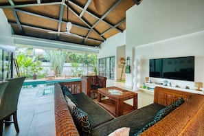 Ein modernes Wohnzimmer mit Pool, Korbmöbeln und einem großen Flachbildfernseher.
