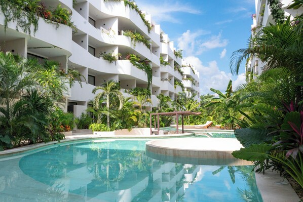 A pool surrounded by lush greenery and a multi-story building with balconies. - Vrbo Property (Tulum)